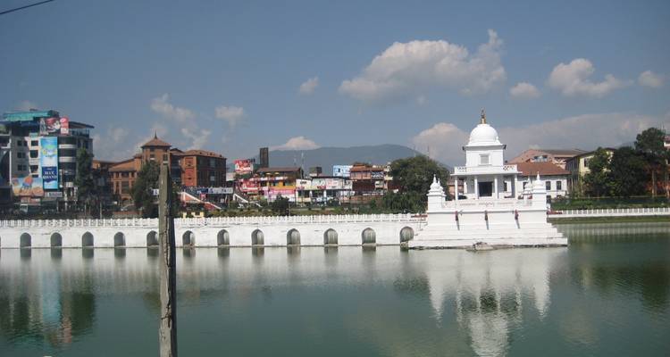 Stupa blanc près d'un plan d'eau réfléchissant sous un ciel clair.