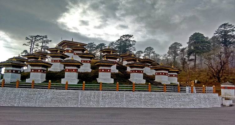Des chörtens alignés par un matin nuageux avec une pente boisée.