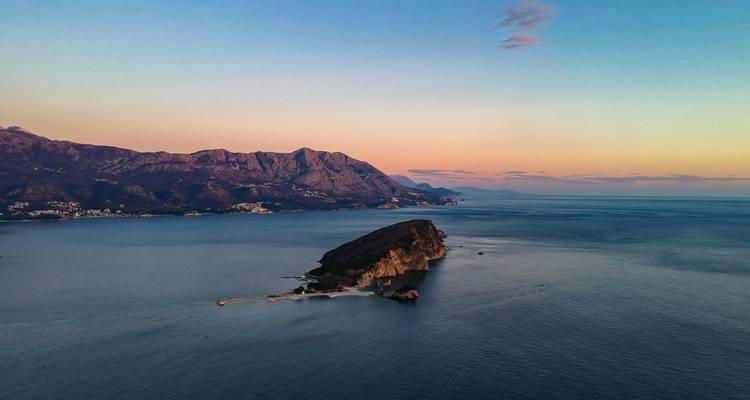 Aerial view of an island with mountains in the background under a sunset sky.