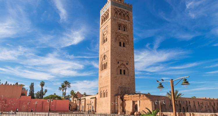 Hoch aufragender Minarett vor einem blauen Himmel in einer belebten Stadtumgebung.