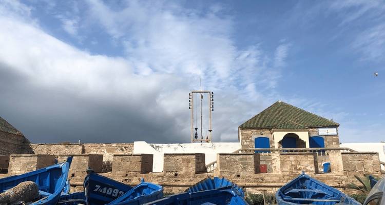 Alte Festung mit blauen Booten davor unter bewölktem Himmel.