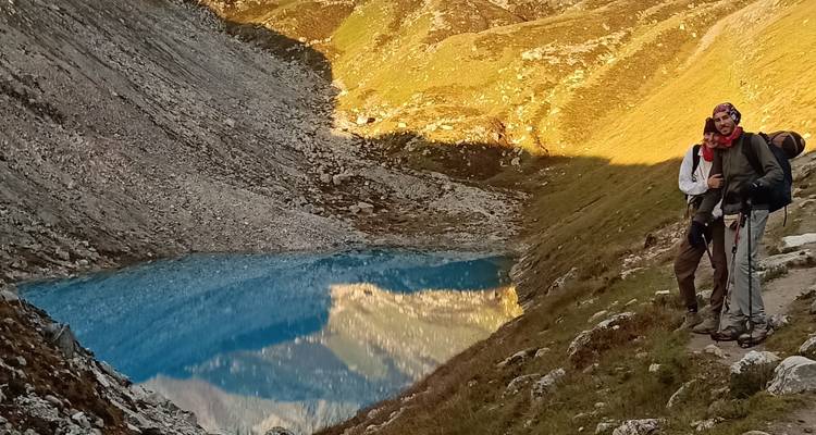 Randonneur debout près d'un lac bleu dans une vallée de montagne au coucher du soleil.