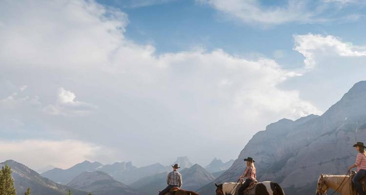 Los vaqueros cabalgan a través de un valle pintoresco enmarcado por imponentes picos de las Montañas Rocosas Canadienses.