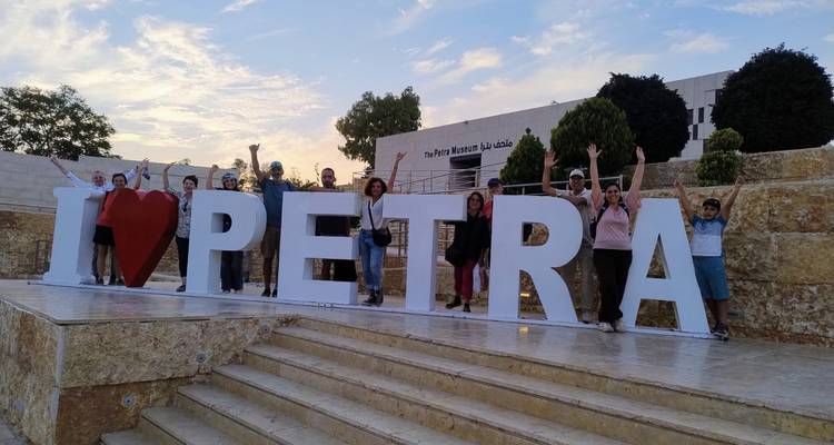 Groupe de personnes posant avec un panneau "J'AIME PETRA" au coucher du soleil.
