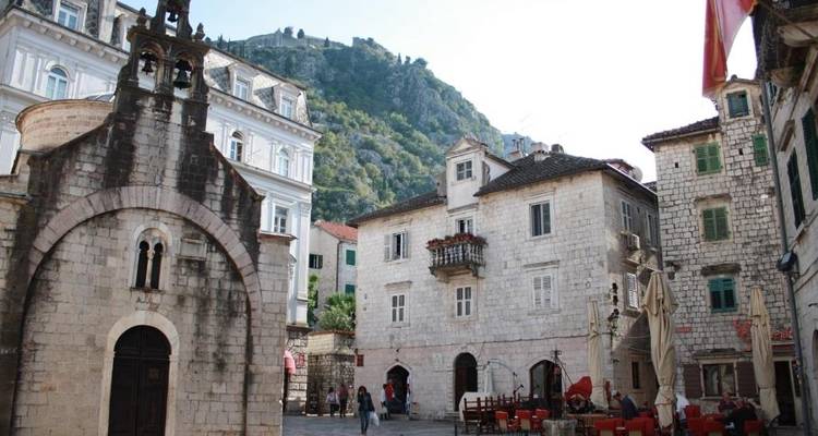 Historic stone square with small church and mountainous backdrop.