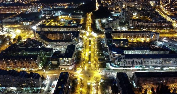 Night aerial view of a lit-up cityscape with streets and buildings.