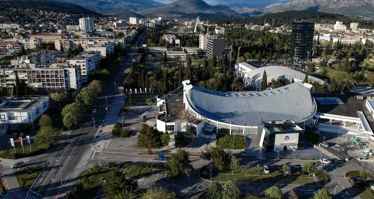 Aerial view of a modern city amid greenery with mountains in the background.