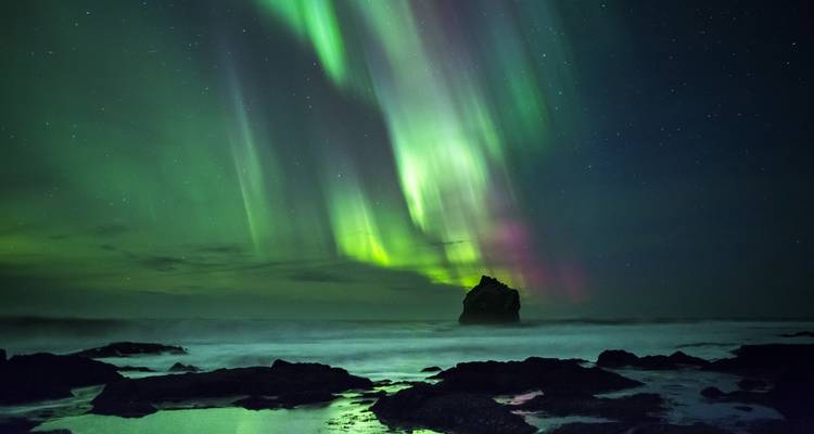 Northern lights over a rocky coastline at night.