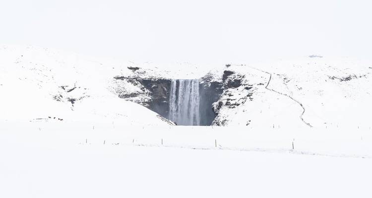 Waterfall in winter landscape with snow covering the surroundings.