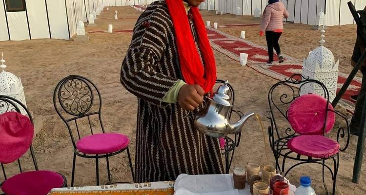 Person serving tea in a desert camp setting.