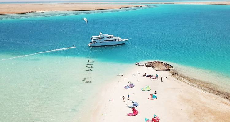 Yacht anchored near a small sandy island with kiteboarders.