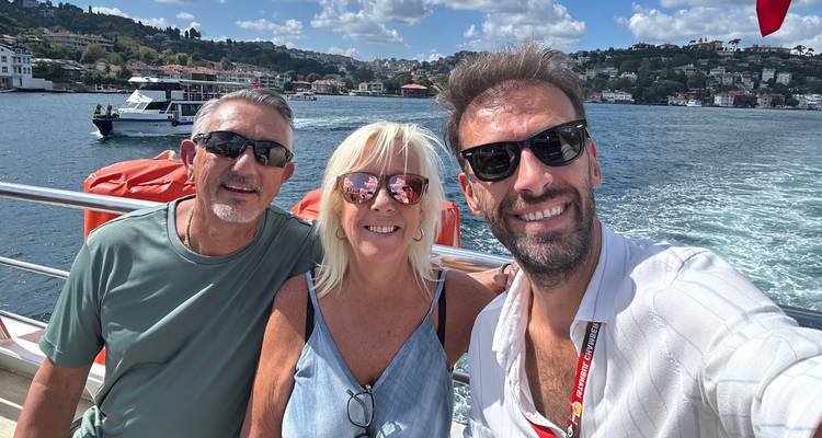 Tres personas tomándose una selfie en un barco con un paisaje urbano de fondo.