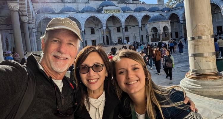 Selfie de tres personas frente a un edificio histórico con cúpulas.