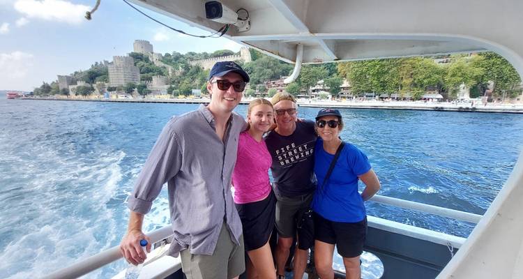 Grupo de personas en un barco con una fortaleza y paisaje urbano al fondo.