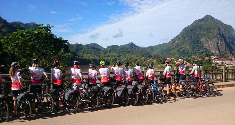 Radfahrer auf einer Brücke mit malerischer Bergkulisse.