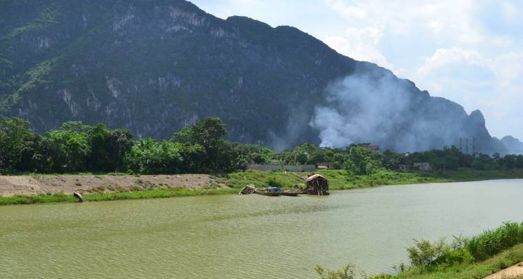 Fluss, der durch eine üppige Landschaft fließt, mit Rauch, der im Hintergrund aufsteigt.
