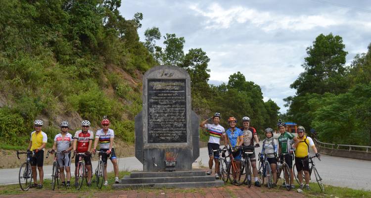 Große Gruppe von Radfahrern, die vor einem Steinmonument posieren.