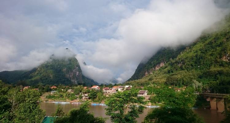 Peaceful village by a river with surrounding green mountains.
