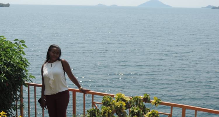 Femme posant près d'un grand lac avec des montagnes au loin.