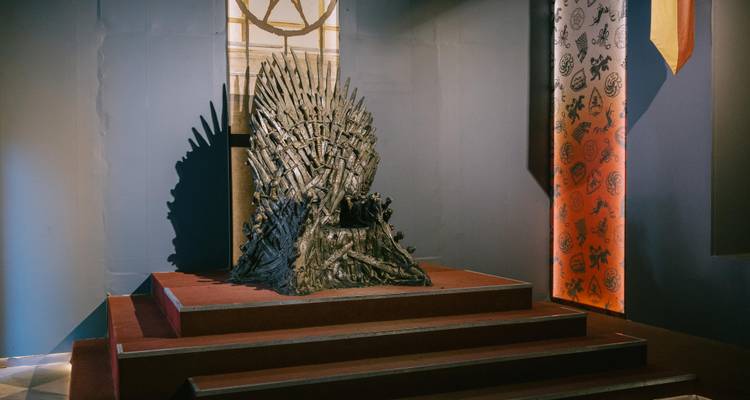 The famous Iron Throne replica displayed on a raised platform inside a dim exhibition room.