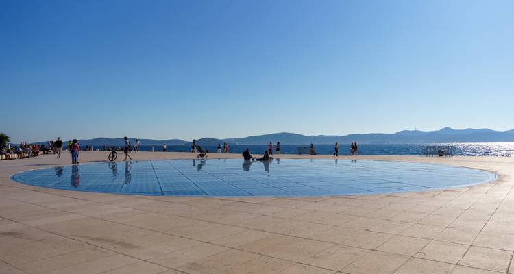 Instalación circular de paneles solares en la costa de Zadar con visitantes descansando junto al Adriático brillante.