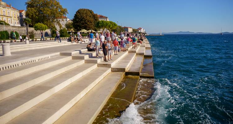 Los escalones del Órgano de Mar en terrazas de Zadar se llenan de visitantes mientras las olas chocan contra el paseo marítimo.
