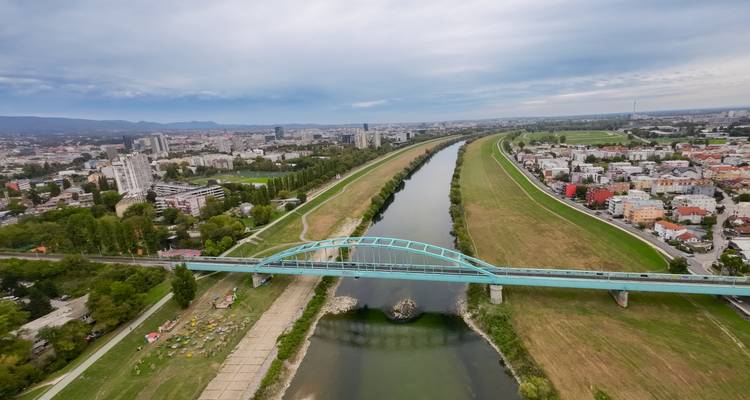Vista aérea de Zagreb mostrando el puente peatonal turquesa sobre el río Sava y el amplio paisaje urbano.