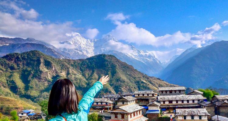 Frau zeigt auf entfernte Berggipfel von einem Dorf aus