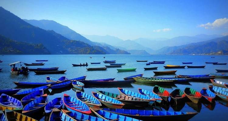 Kleurrijke boten op een meer met bergen op de achtergrond.