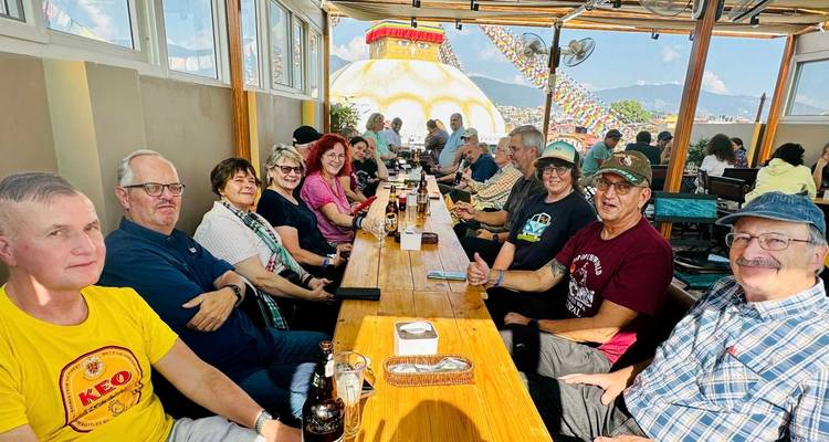 Groep mensen zittend aan een lange tafel met uitzicht op een stupa op de achtergrond.