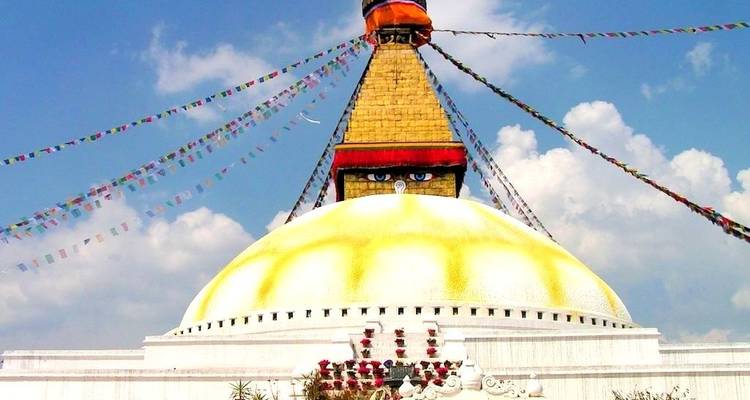 A large stupa with colorful prayer flags under a blue sky.