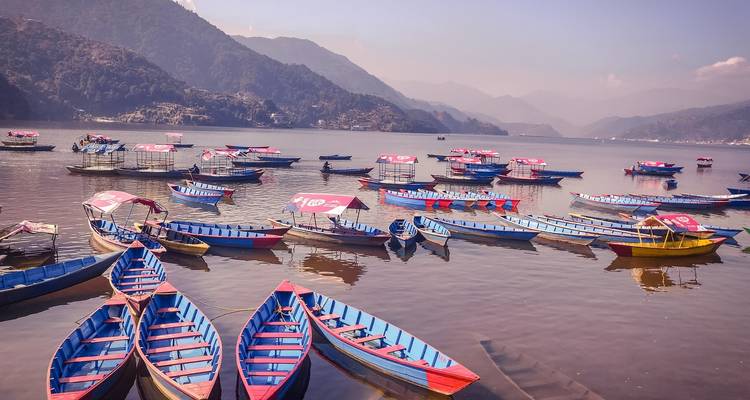 Bunte Boote auf einem ruhigen See mit bergiger Umgebung.