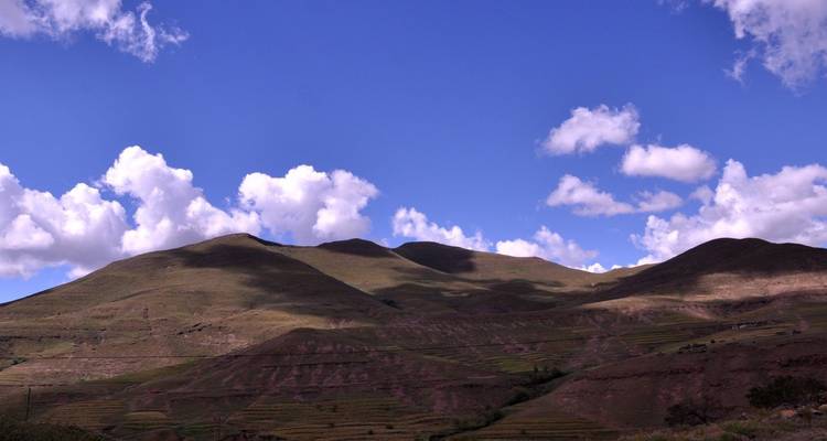 Montañas verdes y ondulantes bajo un cielo azul profundo salpicado de nubes blancas brillantes.