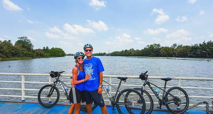 Couple de cyclistes portant des casques posant sur le pont d'un ferry au-dessus d'un large chenal du fleuve Mékong.
