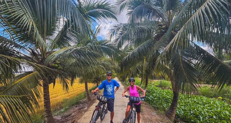 Les cyclistes se tiennent sur un sentier étroit bordé de grands cocotiers et de rizières dorées.