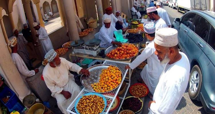 Escena de mercado local con hombres vestidos con ropa tradicional vendiendo frutas.