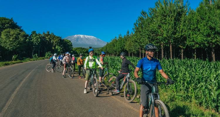 Group of cyclists stopped on a road with Mount Kilimanjaro in the background.