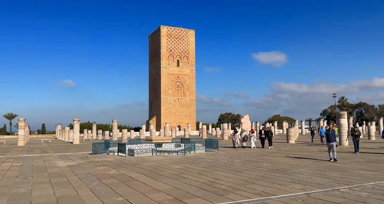 Toeristen verkennen de esplanade van Rabat's Hassan Toren omringd door marmeren zuilen onder een heldere hemel.