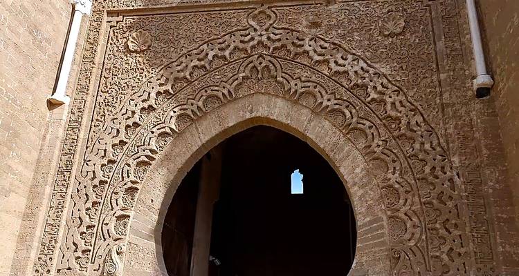 Gedetailleerde steenbewerking omringt een grootse gewelfde deuropening in een oude Marokkaanse fortificatie.