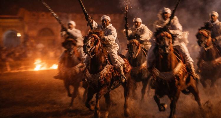Plan d'action flou de cavaliers marocains traditionnels exécutant une fantasia de nuit avec des flammes.