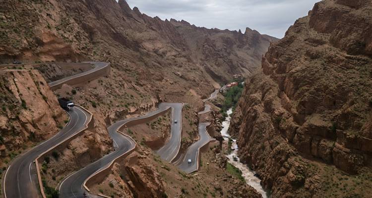 Route sinueuse spectaculaire taillée dans les parois escarpées du canyon le long d'une rivière tumultueuse sous un ciel couvert.