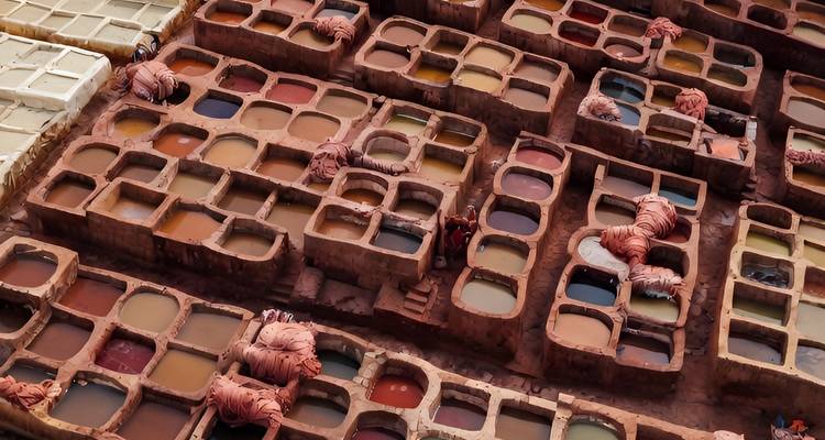 Vue à vol d'oiseau de la tannerie de Fès avec des fosses de teinture multicolores et des ouvriers au milieu de piles de cuir.