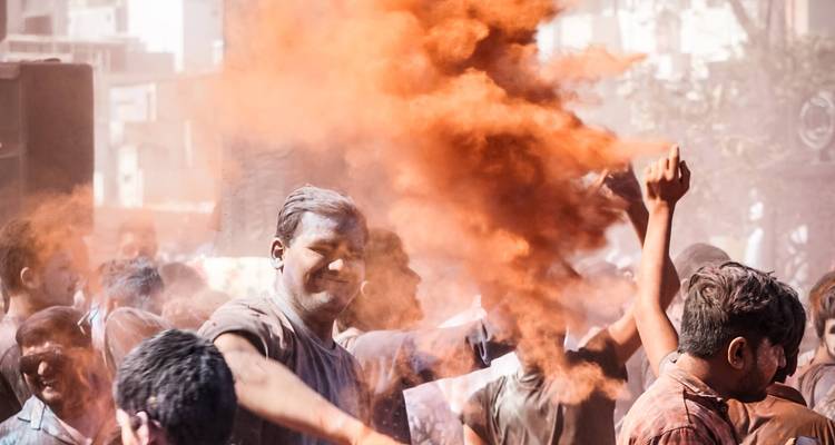 Gente lanzando polvo naranja de Holi al aire.