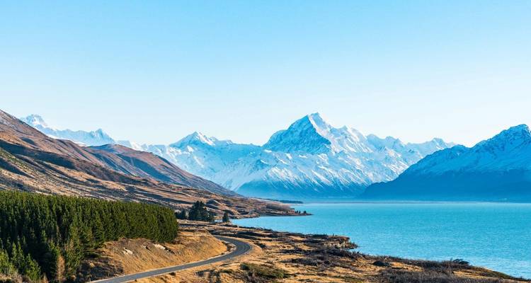 Montagnes enneigées avec un lac au premier plan et un ciel bleu dégagé.