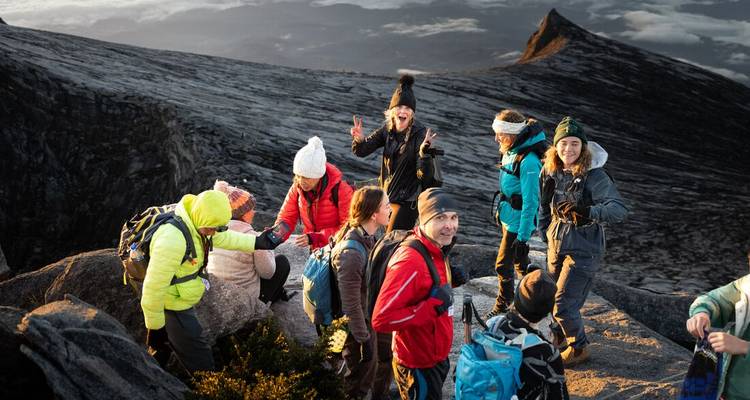 Excited hikers in colorful gear posing on rocky Mount Kinabalu slopes at sunrise.