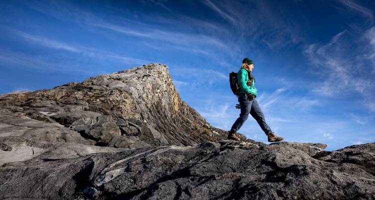 Solo trekker in green jacket walking across a rocky ridge under a vibrant blue sky.