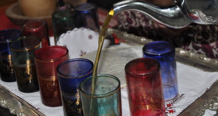 A silver teapot pouring tea into glasses of various colors.