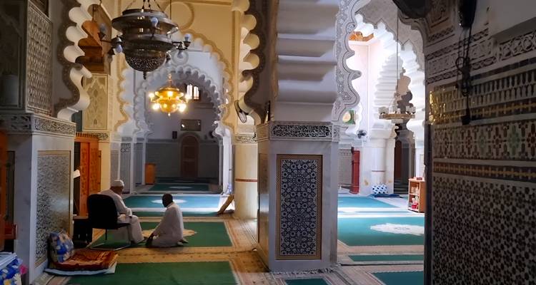 Twee mannen bidden in een prachtig versierde moskee met geschulpte bogen en groen tapijt.
