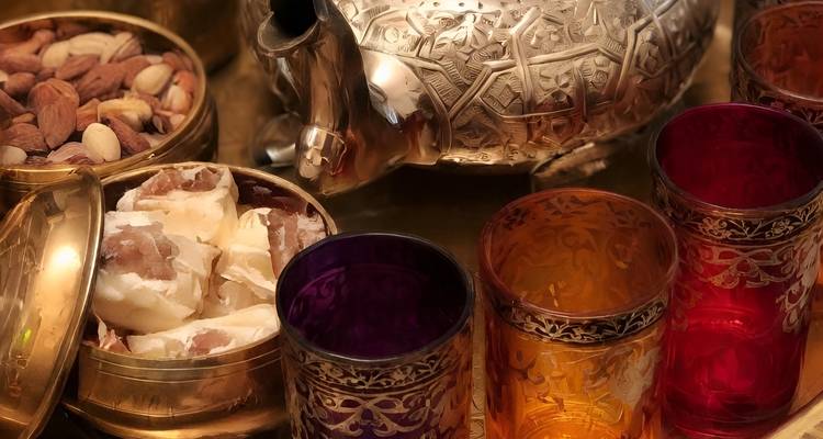 Gros plan de verres à thé marocains ornés, noix et théière en argent sur un plateau en laiton