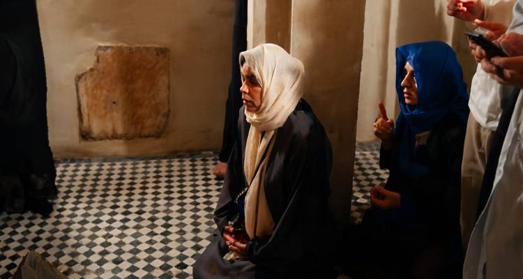 Femmes en foulards assises sur un sol en mosaïque à l'intérieur d'un bâtiment historique marocain.